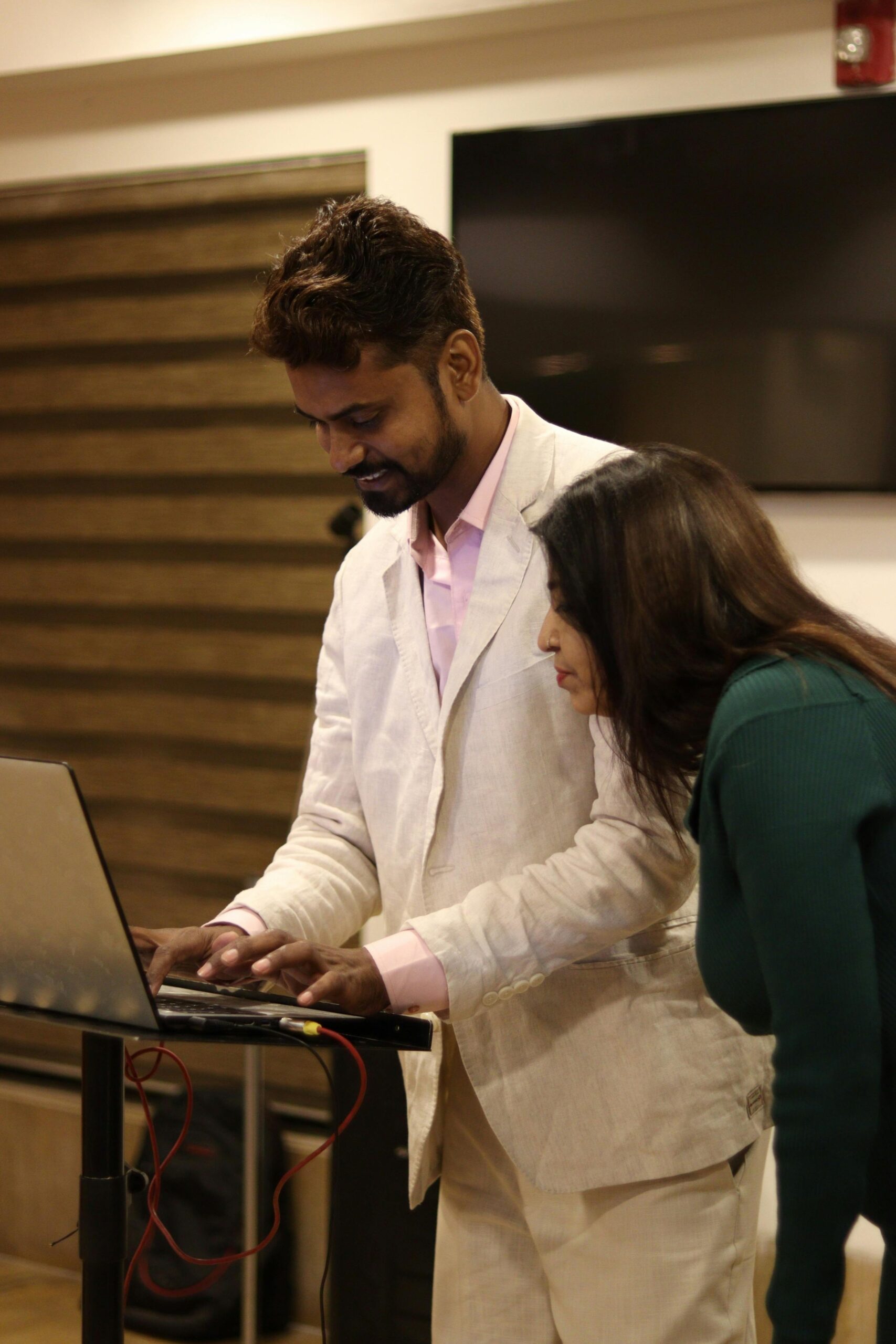 Two professionals collaborate on a project using a laptop in an indoor office setting.