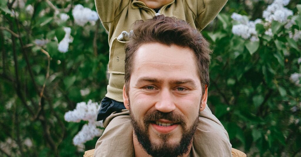 Happy father carrying son on shoulders in a blooming garden setting.